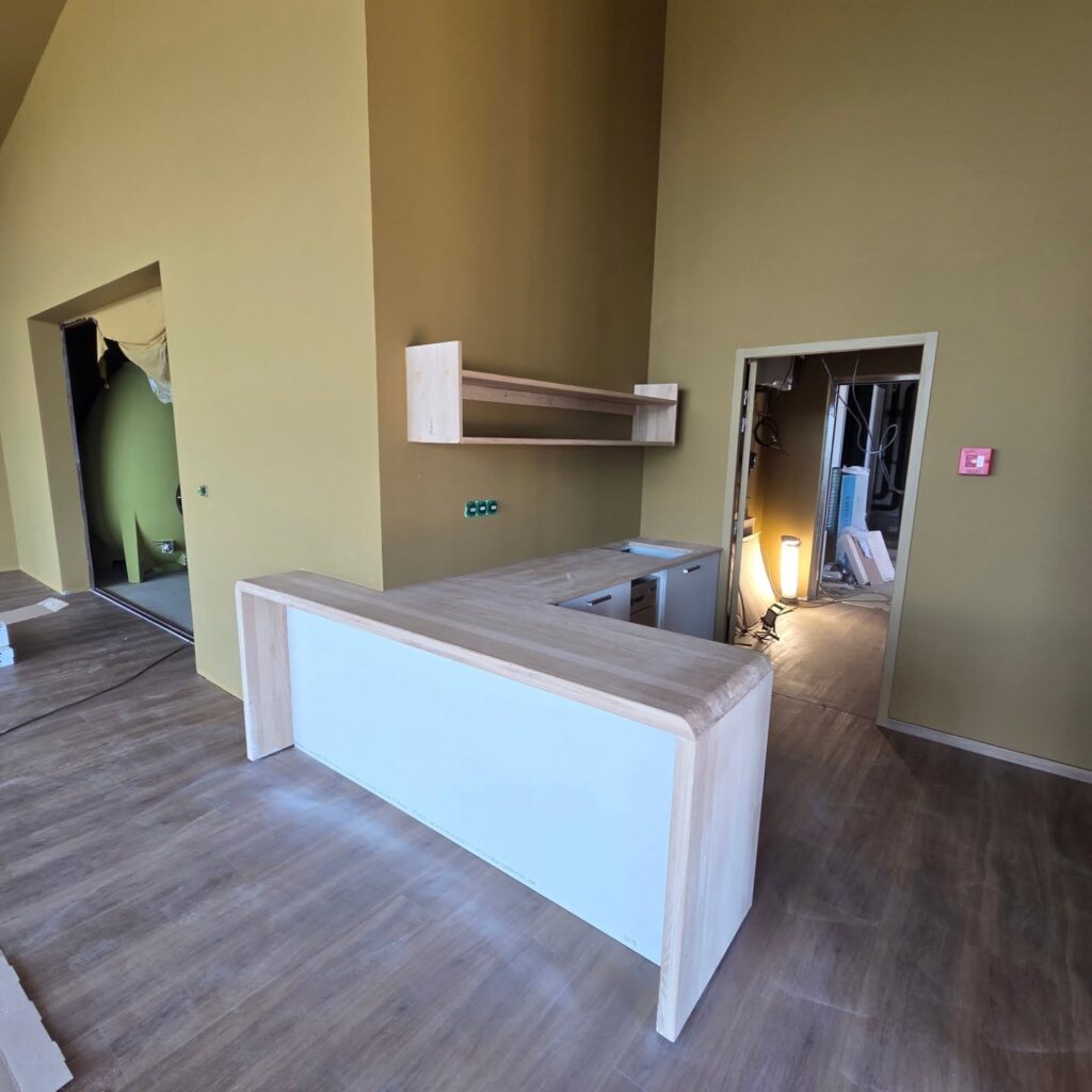 Rénovation Moderne : Comptoir Bois, Murs Ocre et Déco Espace intérieur en rénovation avec un comptoir en L bois clair et blanc. Murs ocre, sol effet bois. Une grande cuve verte et un chantier visible.